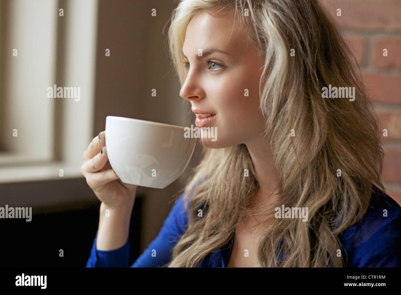 Schöne lächelnde junge Frau mit langen Haaren, genießen Sie ihren Cappuccino in einem Café Stockfoto