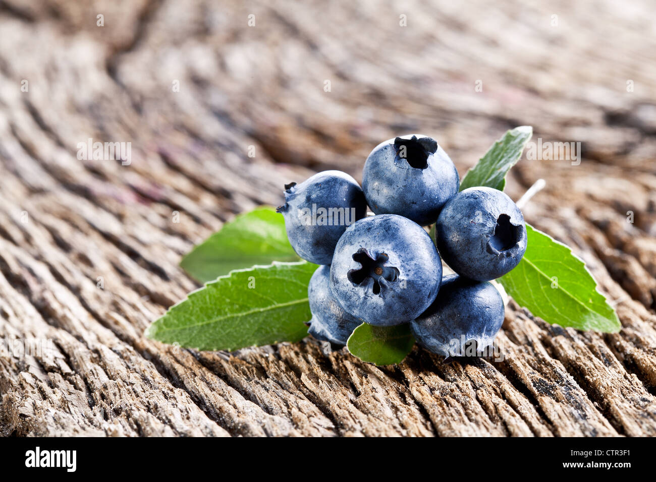 Heidelbeeren mit Blättern auf einem alten Holztisch. Stockfoto