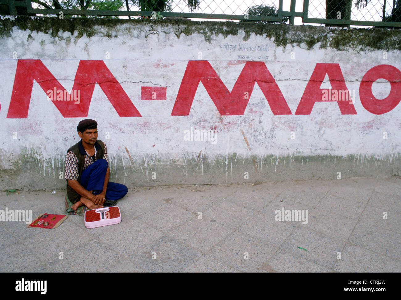 In einer Straße, ein Mann mit einem Gleichgewicht wartet auf Passanten, die sich zu wiegen. Hinter ihm, MAO geschrieben steht an einer Wand (Nepal) Stockfoto