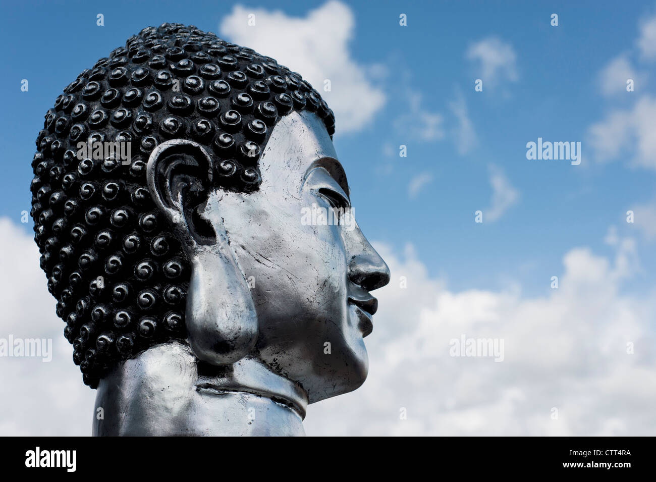 Profil von Silber-Buddha-Kopf vor einem bewölkten blauen Himmel Stockfoto