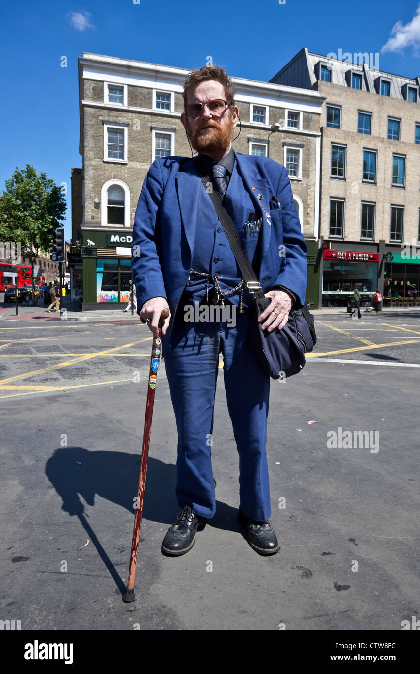 Ganzkörperportrait eines bärtigen Mannes, der mit einem Gehstock auf einem Bürgersteig steht, London, England, Großbritannien. Stockfoto