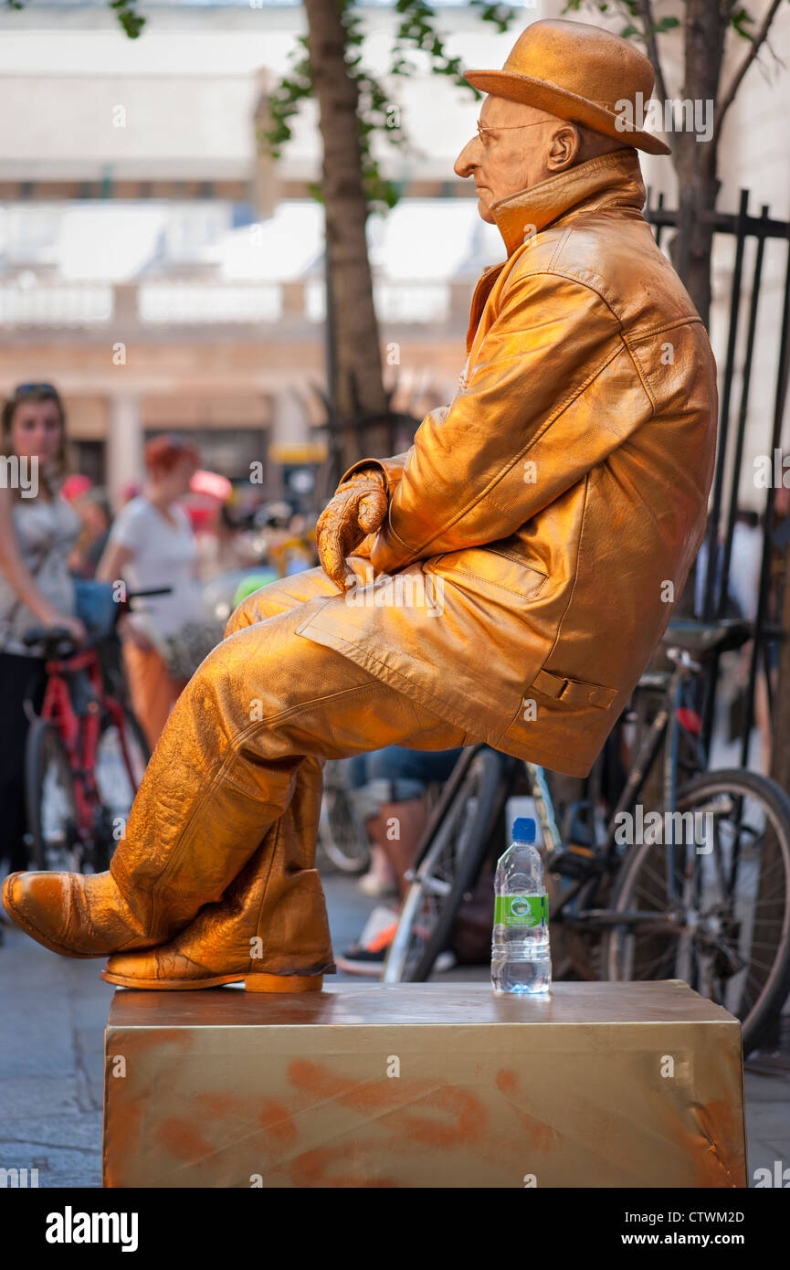 London Covent Gardens Market Street Entertainer busker mime Artist in goldenen Sitzen sitzt auf Luft von Touristen & Kinder aufgepasst Stockfoto