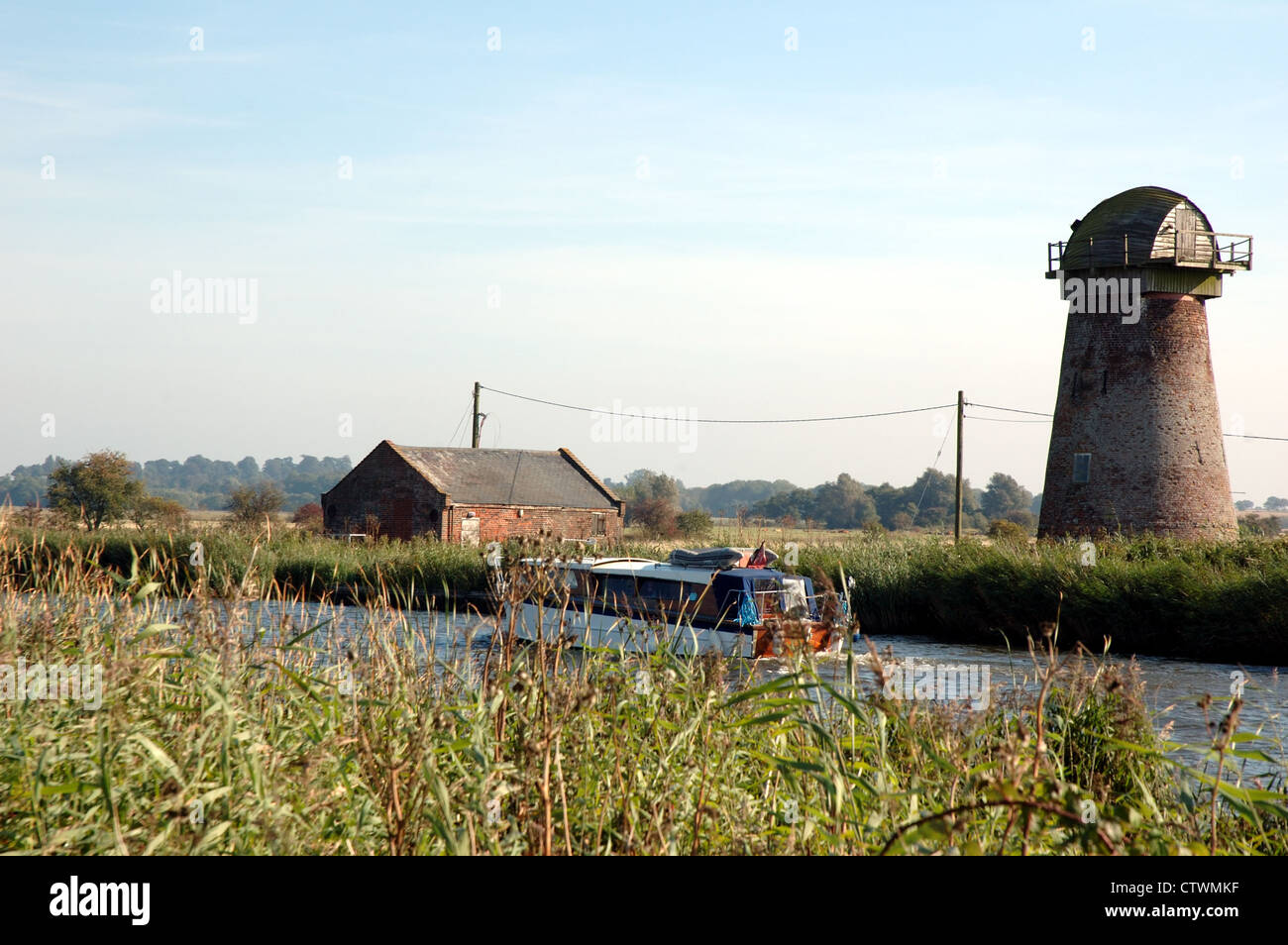 Traditionellen hölzernen Broads Cruiser auf dem Fluss Bure mit verfallenen Clippesby Mill am gegenüberliegenden Ufer, Broads National Park Stockfoto