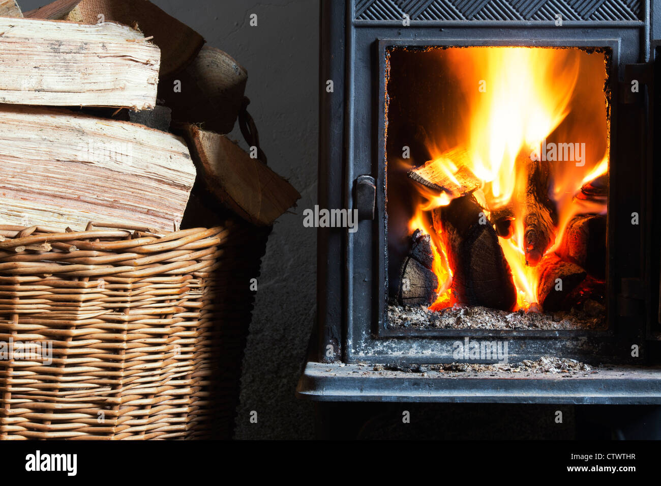 Holz Brennen in einem Kaminofen und einen Korb von Protokollen. Großbritannien Stockfoto