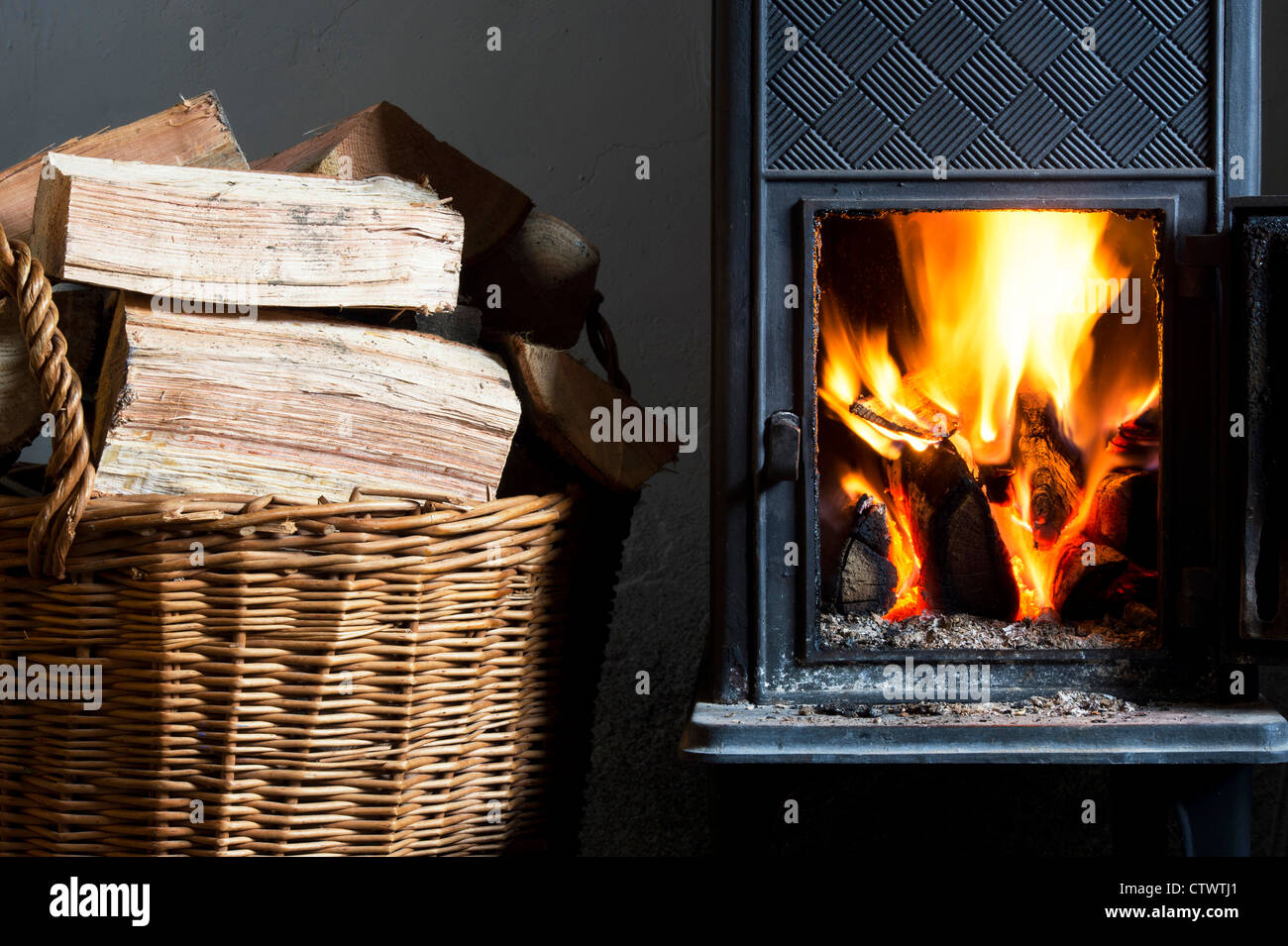 Holz Brennen in einem Kaminofen und einen Korb von Protokollen. Großbritannien Stockfoto