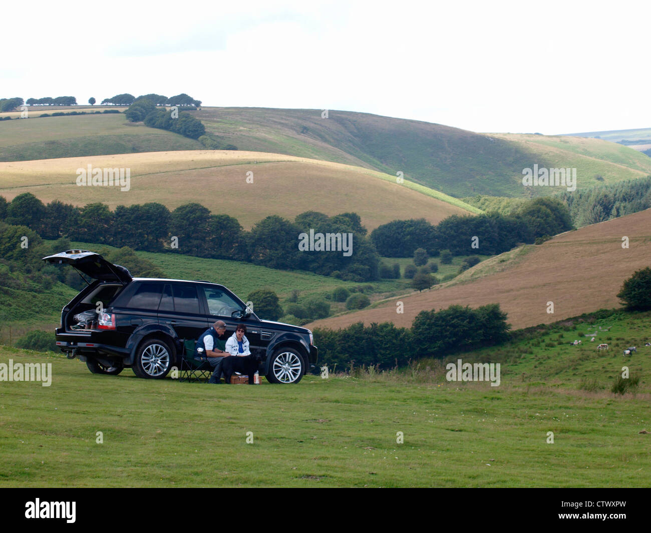 Paar saß neben Range Rover mit einem Picknick, Exmoor, Großbritannien Stockfoto