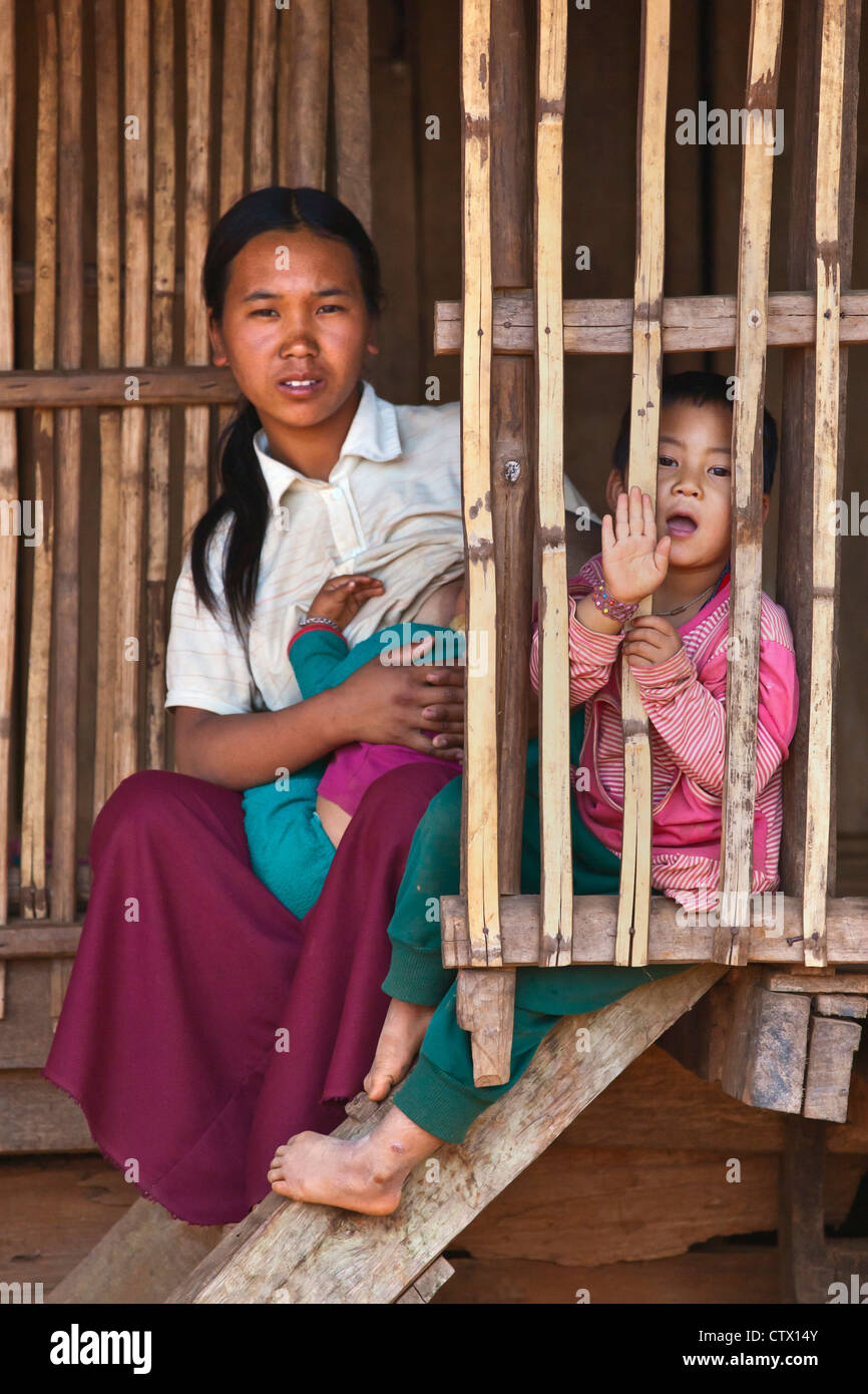 Frauen des Stammes AKHA Krankenschwestern ein Kind in ihrem Bambus Haus - Dorf in der Nähe von KENGTUNG oder KYAINGTONG - MYANMAR Stockfoto