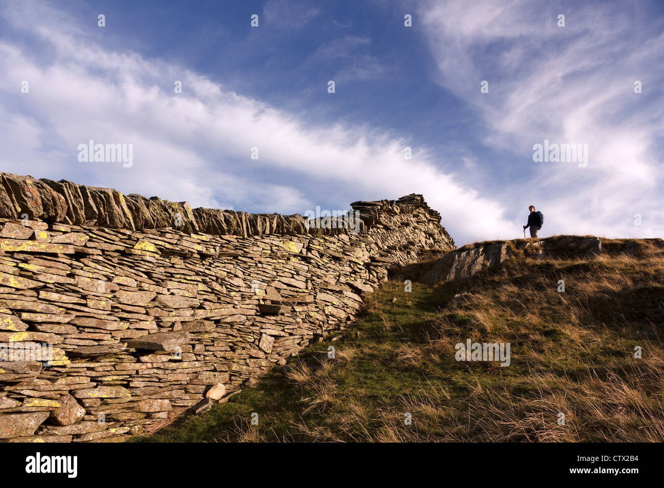 Einsamer Wanderer an einer alten Schieferwand auf Lingmoor fiel gegen den blauen Himmel mit Cirrus Wolken, Lake District, Cumbria, England, Großbritannien Stockfoto