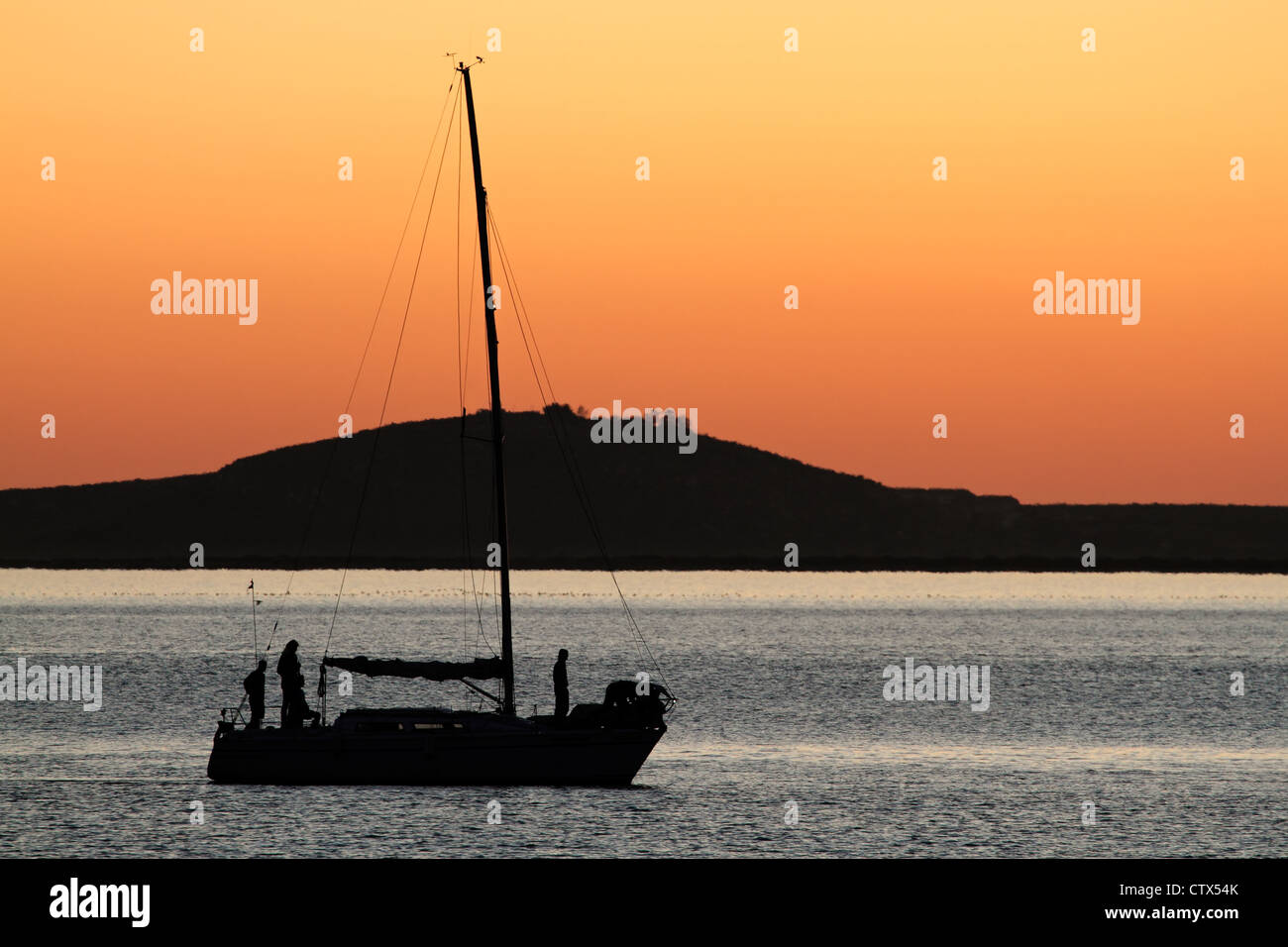 Silhouette einer Yacht gegen einen roten Sonnenuntergang mit reflektierenden Wasser Stockfoto