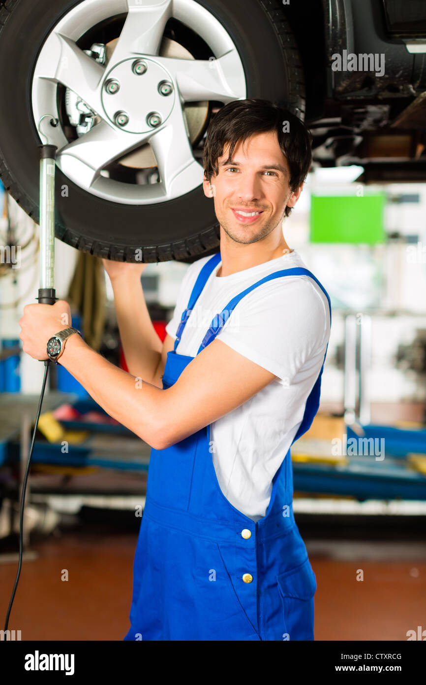 Junger Mann im blauen overall - Mechaniker - Arbeit mit Lampe auf dem Auto  aufgebockt in einer Tankstelle Stockfotografie - Alamy