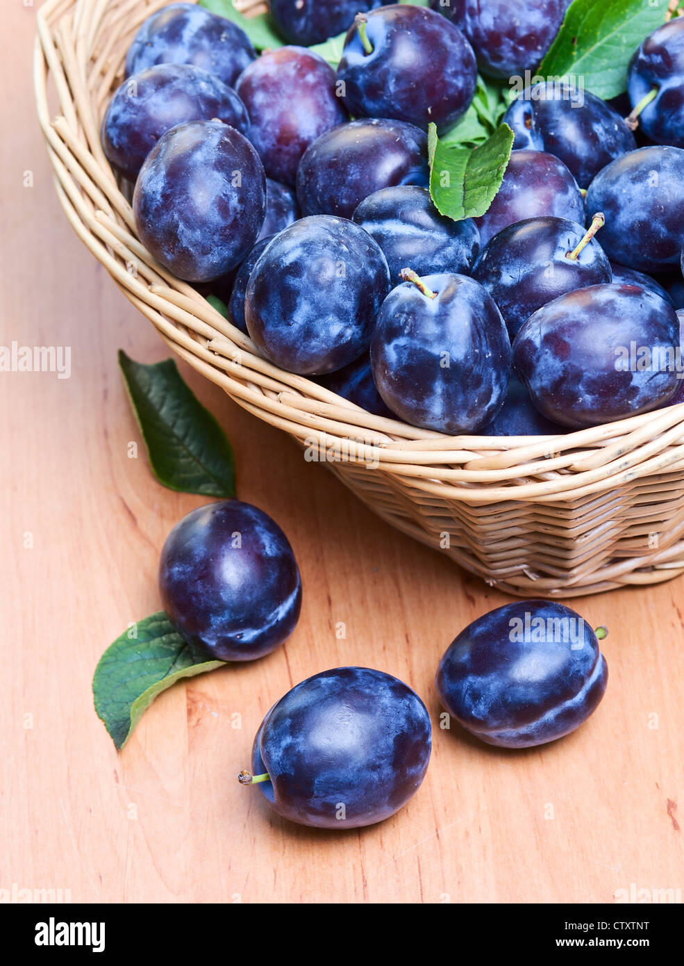 reife Pflaumen in Korb auf einem Holztisch Stockfoto