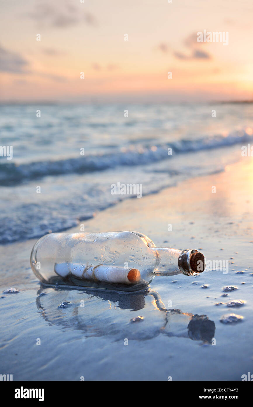 Eine Flaschenpost am Sandstrand bei Sonnenuntergang Stockfoto