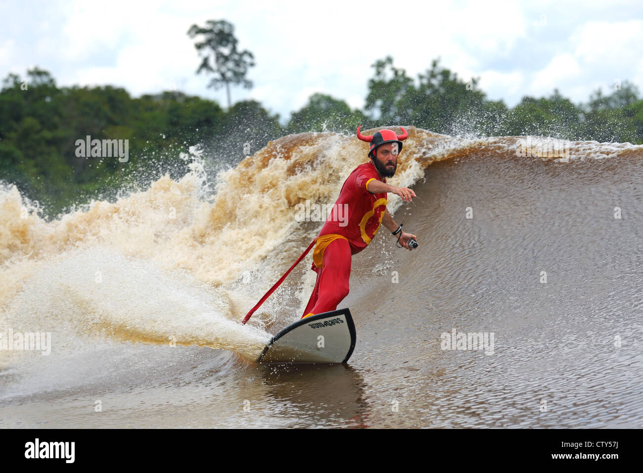 Surfer in roten Superhelden Kostüm Surfen einen Gezeiten-Fluss Bohrung Welle als die Bono oder 7 Geister durch Reisen Surfern bekannt. Stockfoto