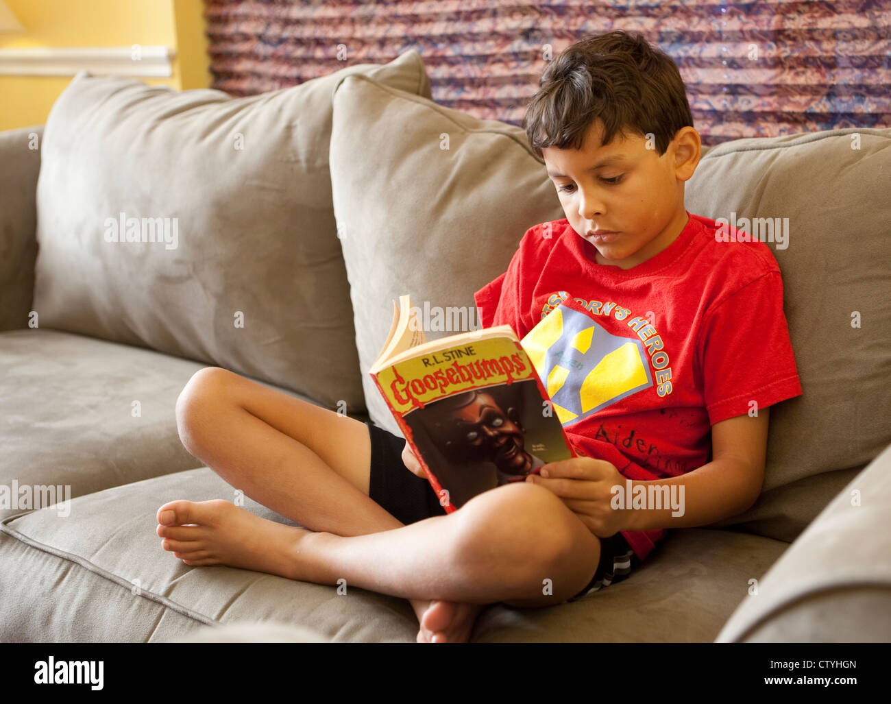Junge 8 Jahr alt mexikanisch-amerikanischen jungen liest softcover Buch, während Sie gemütlich auf dem Sofa zu Hause Stockfoto