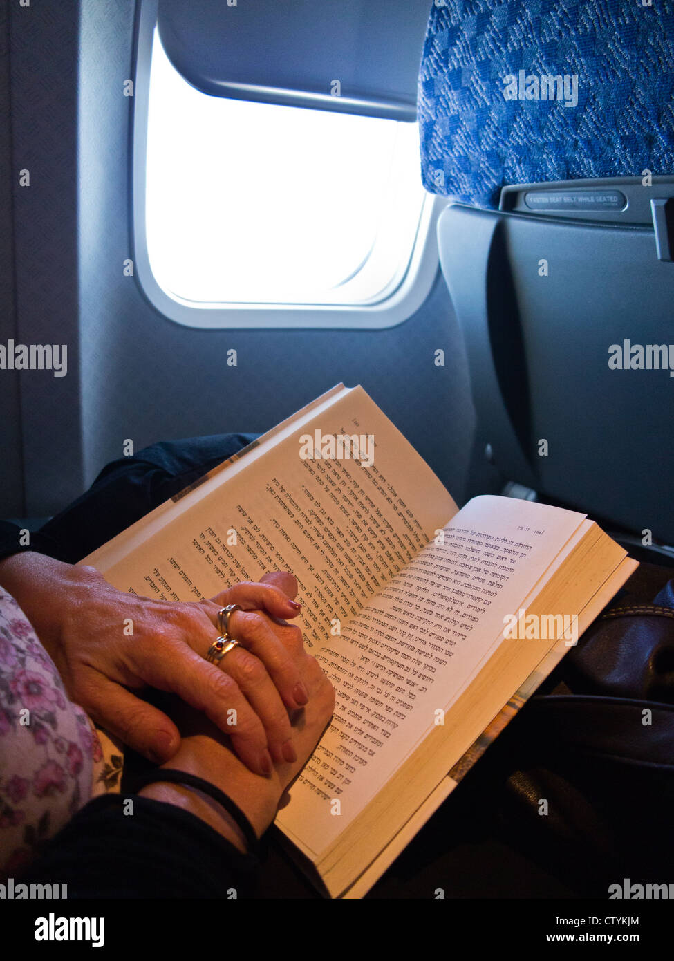 Eine Frauenhand halten ein Buch in Hebräisch, wie sie an Bord eines Flugzeugs liest. Stockfoto