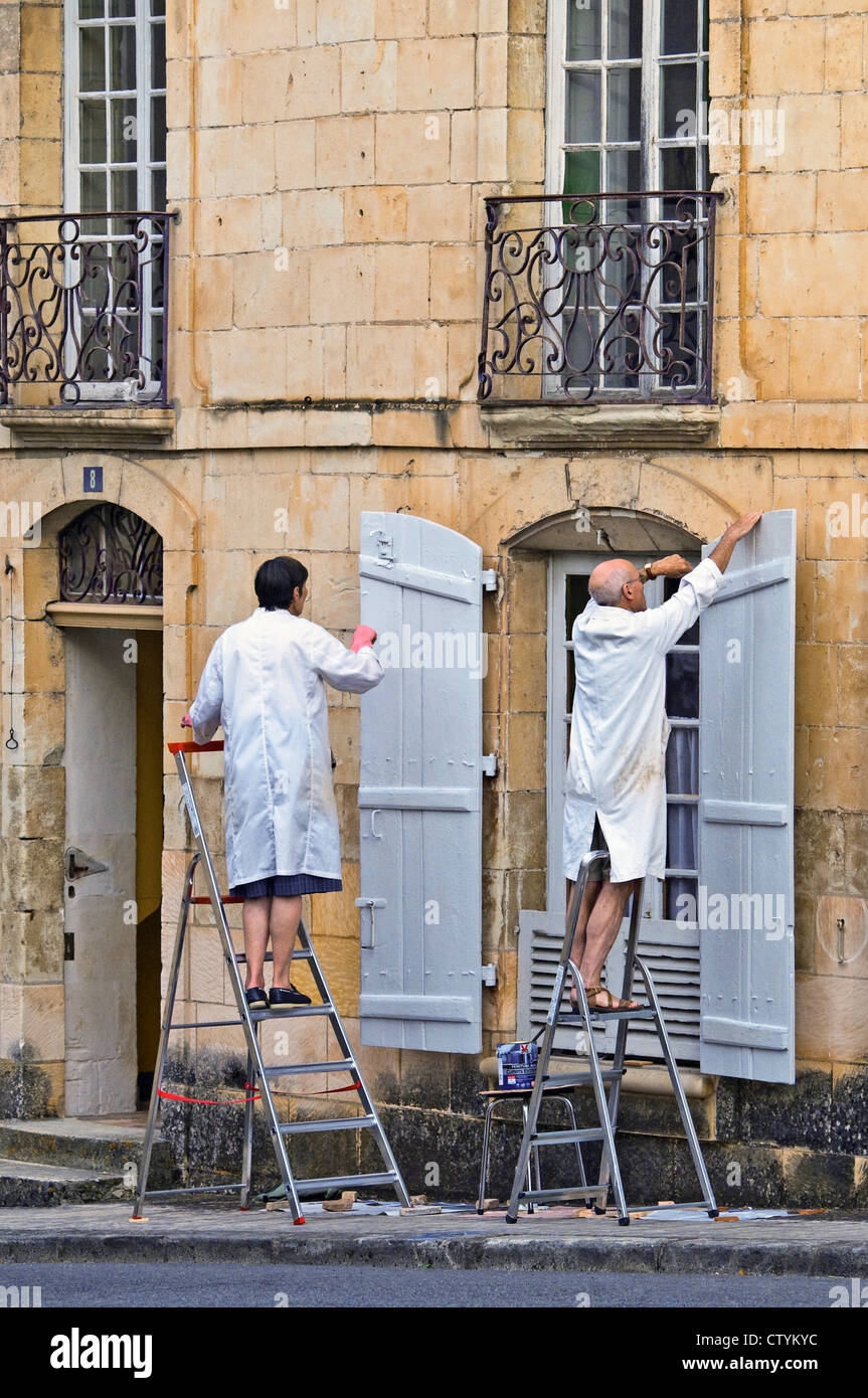 Älteres Ehepaar in Arbeit-Mäntel Malerei Fensterläden - Frankreich. Stockfoto