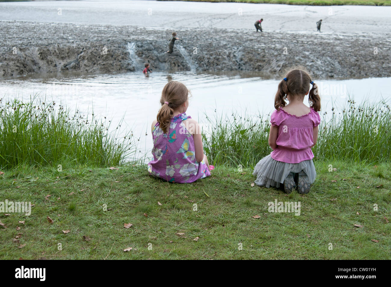 Zwei kleine Mädchen beobachten Kinder spielen in der Mündung Schlamm an den Port Eliot literarische Festival St deutschen Cornwall UK Stockfoto