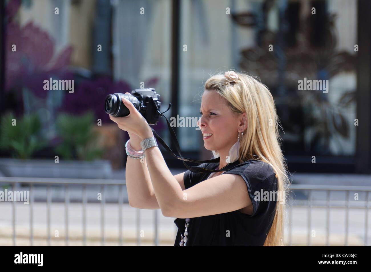 Schöne junge Fotografin mit langen blonden Haaren und schwarzen Kleid fotografieren mit einer DSLR NIKON D5000 18-55 mm Objektiv Stockfoto