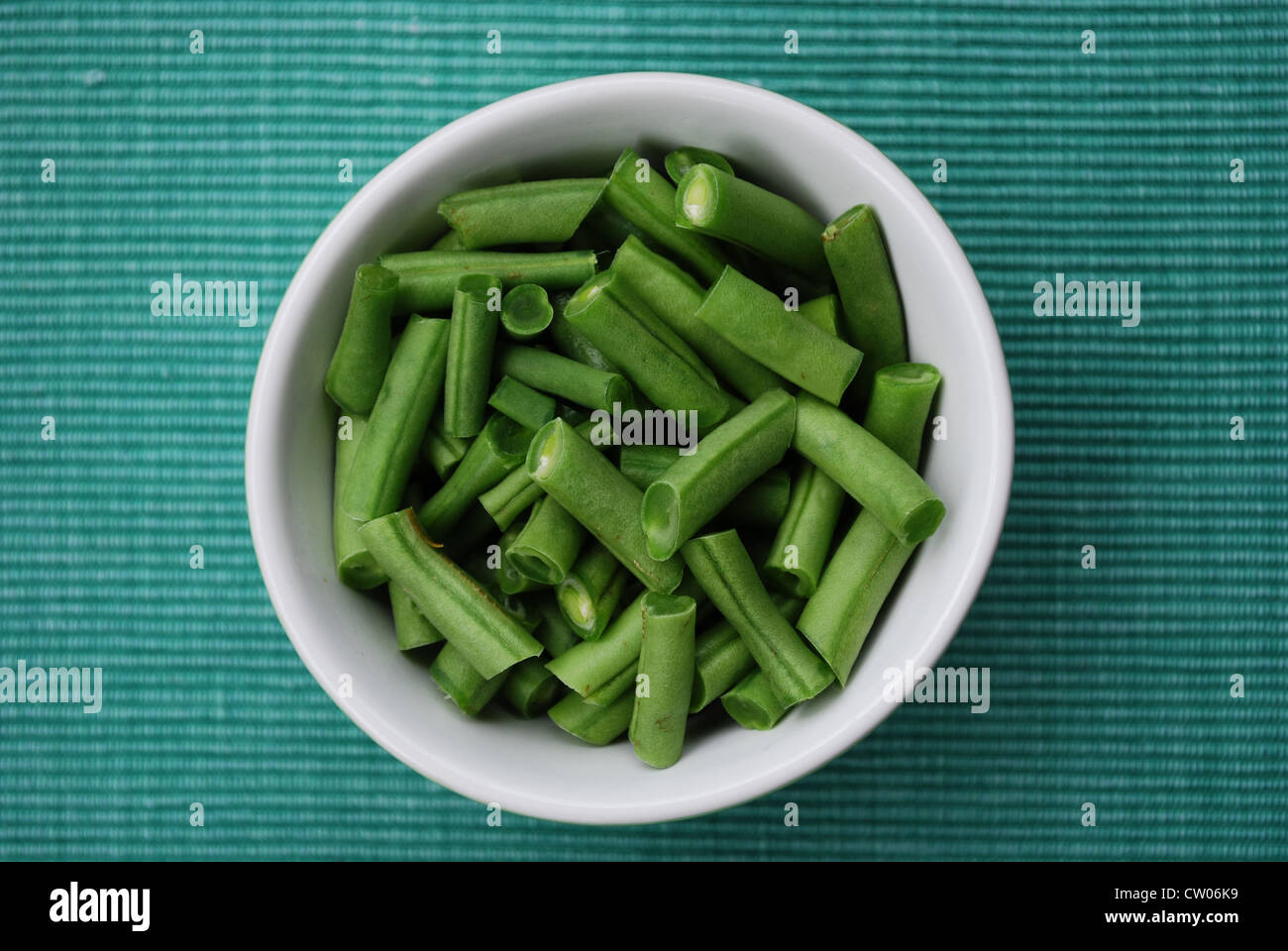 Frischen rohen grünen Bohnen in einer Keramikschale auf grünem Stoff Hintergrund Stockfoto