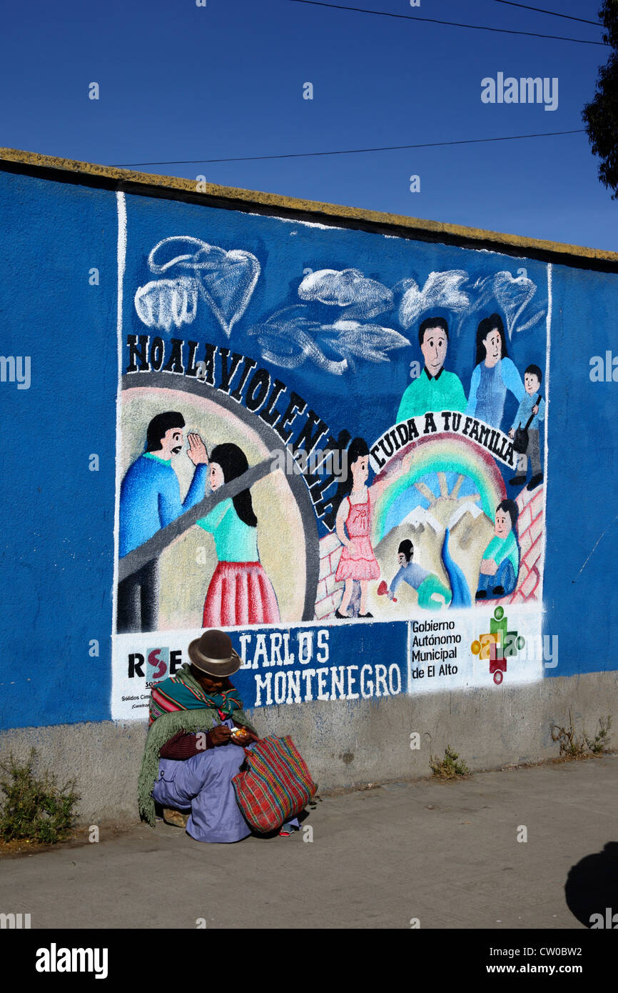 Die gebürtige Frau sitzt auf dem Bürgersteig neben einem Wandgemälde, das Teil einer Kampagne zur Reduzierung von häuslicher Gewalt gegen Frauen ist, El Alto, Bolivien Stockfoto