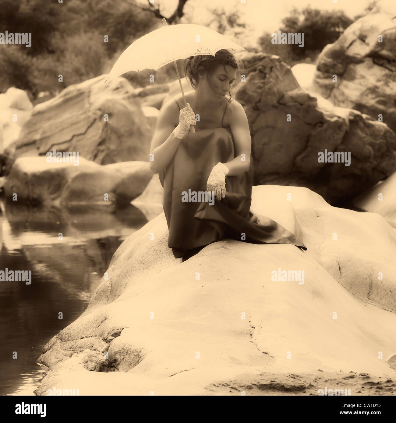 Eine junge Frau sitzt auf einem Felsen im Wasser mit einem Sonnenschirm Stockfoto