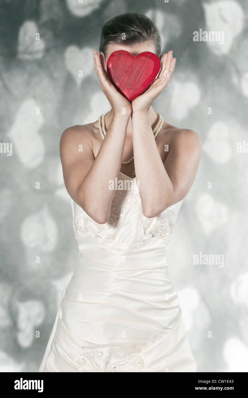 eine Frau in einem Hochzeitskleid hält ein Herz vor dem Gesicht Stockfoto