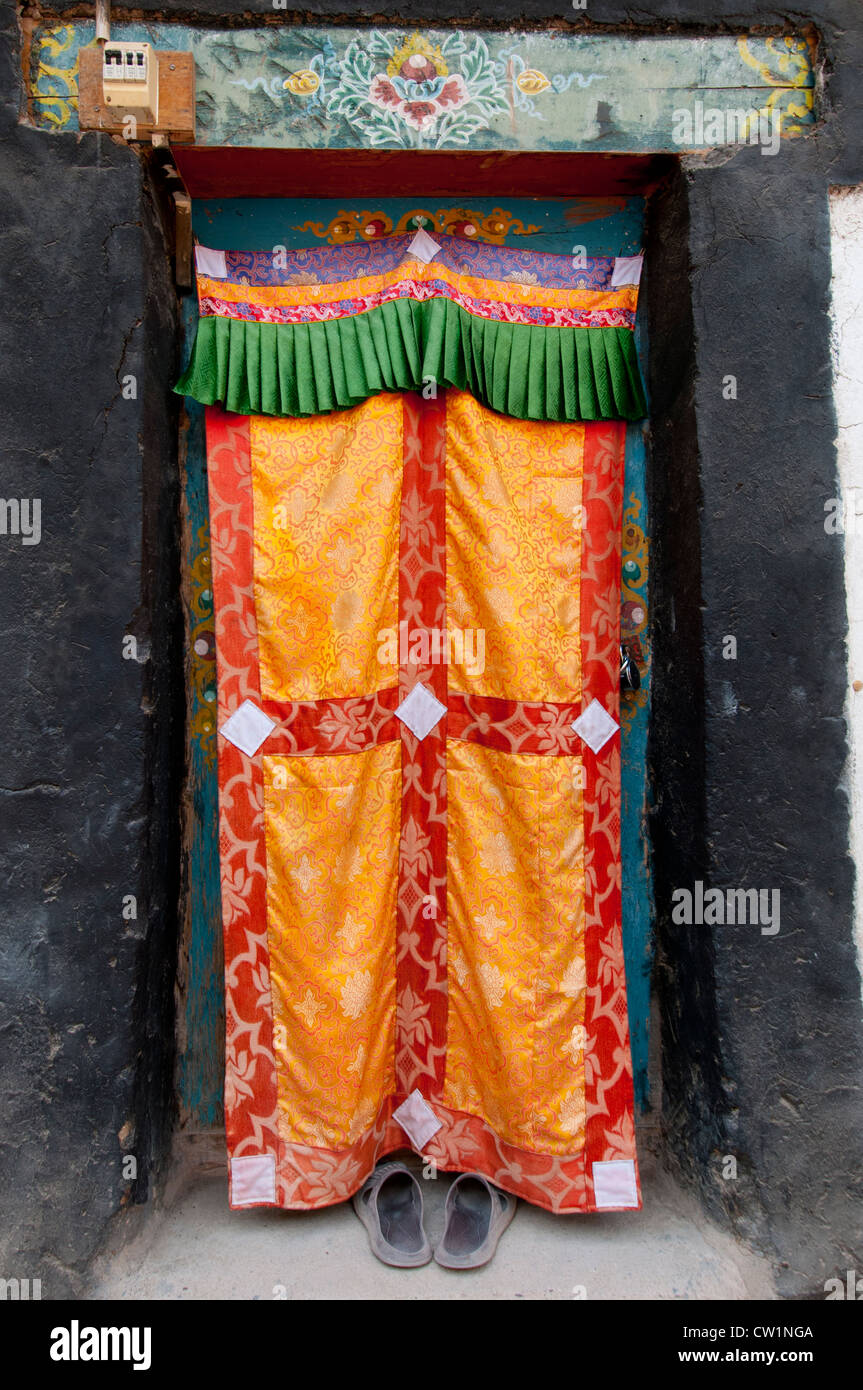 Eine Tür im Hemis Kloster, Ladakh Indien, abgedeckt durch eine bunte Seide Vorhang mit ein paar Croc Schuhe zeigen Stockfoto