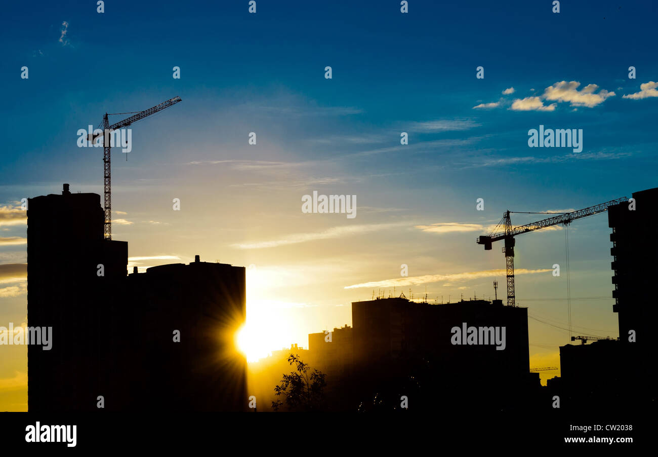 Industrielle Baukräne und Gebäude Silhouetten über Sonne bei Sonnenaufgang Stockfoto
