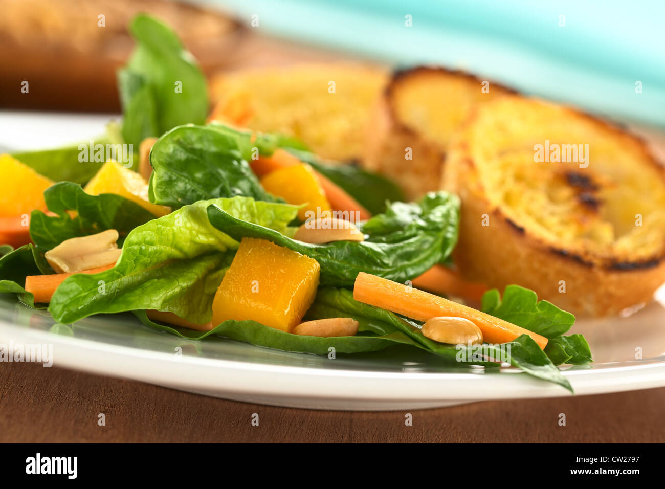 Frischer Spinat, Mango und Karotten-Salat mit Erdnüssen auf Top und gebratenem Baguette Scheiben hinten Stockfoto