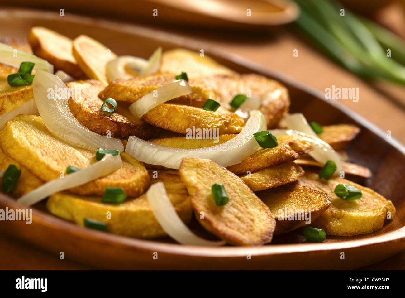 Frische hausgemachte knusprig gebratene Kartoffel-Scheiben mit gebratenen Zwiebeln und Lauch auf Holzplatte Stockfoto