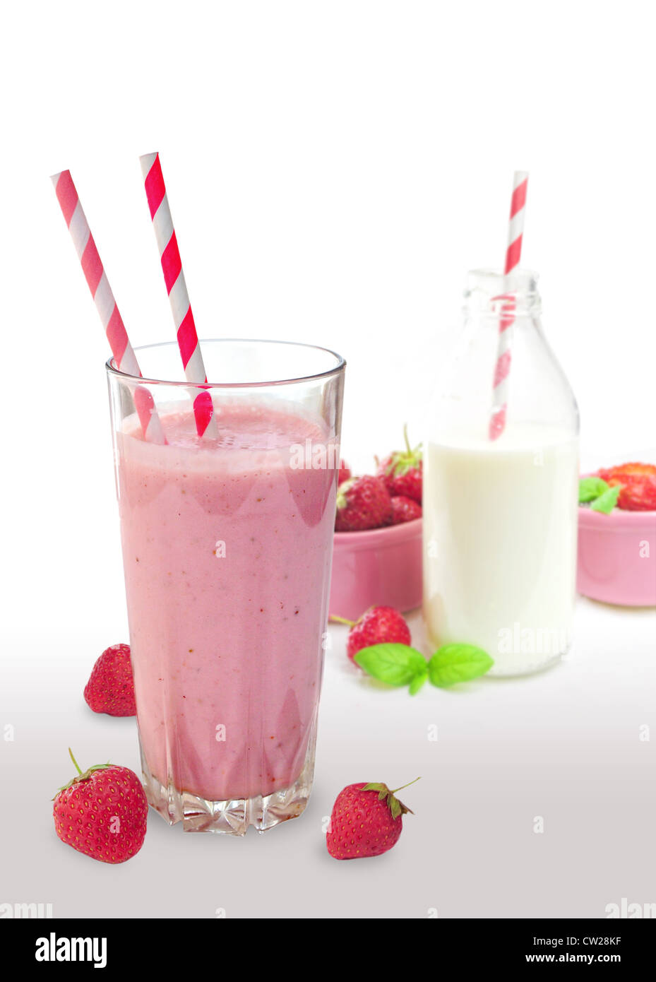 Erdbeer Smoothie aus Glas mit Strohhalmen, eine Flasche Milch und Früchte im Hintergrund Stockfoto