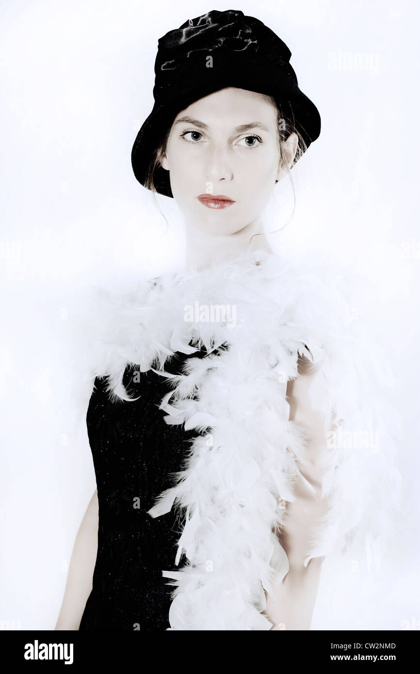eine junge Frau in einem eleganten schwarzen Kleid mit Hut und Federboa Stockfoto
