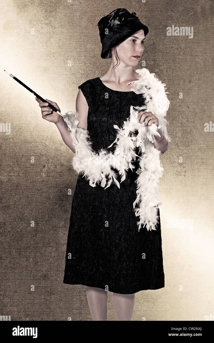 eine Frau in einem schwarzen Kleid mit Federboa und Zigarettenspitze Stockfoto