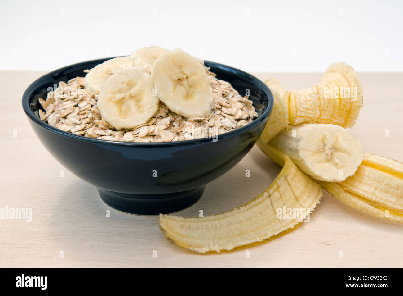 Hafer oder Haferflocken Brei mit in Scheiben geschnittenen Bananen an der Spitze in schwarz Schüssel und Banane von der Seite gerollt Stockfoto
