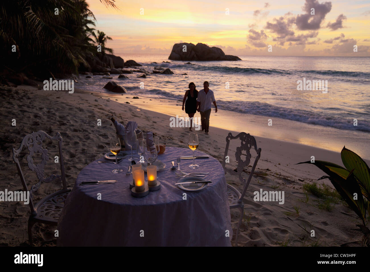 Romantisches Paar Spaziergang bei Sonnenuntergang am Strand mit Esstisch im Vordergrund. Cousine Island.Seychelles Stockfoto
