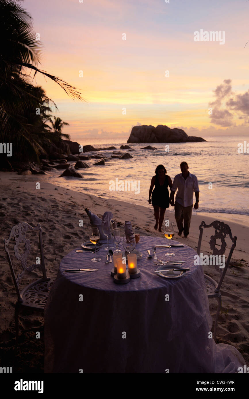Romantisches Paar Spaziergang bei Sonnenuntergang am Strand mit Esstisch im Vordergrund. Cousine Island.Seychelles Stockfoto