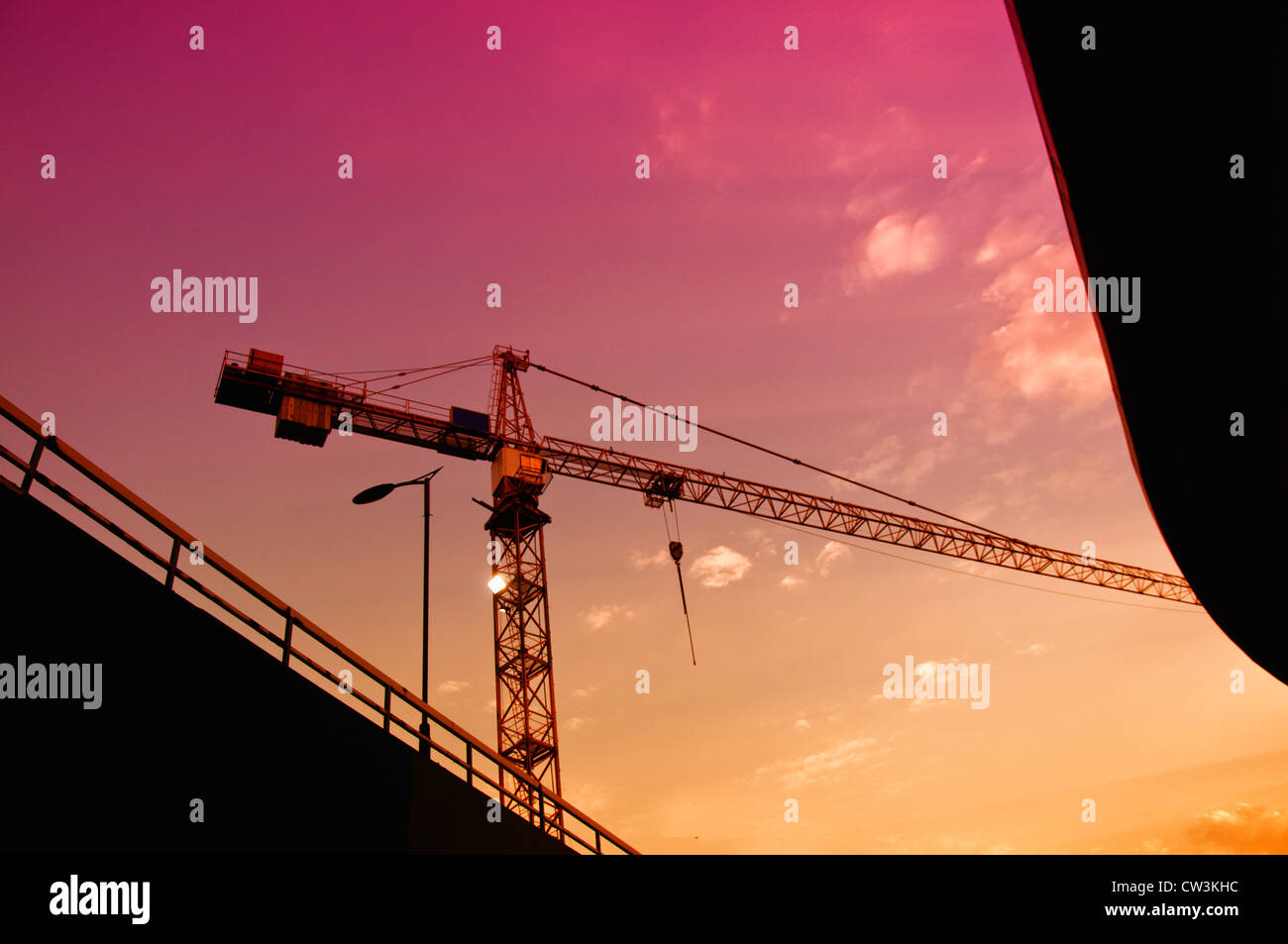 Silhouetten der Baukran und eine Brücke in Dämmerung gegen den bunten Himmel. Stockfoto