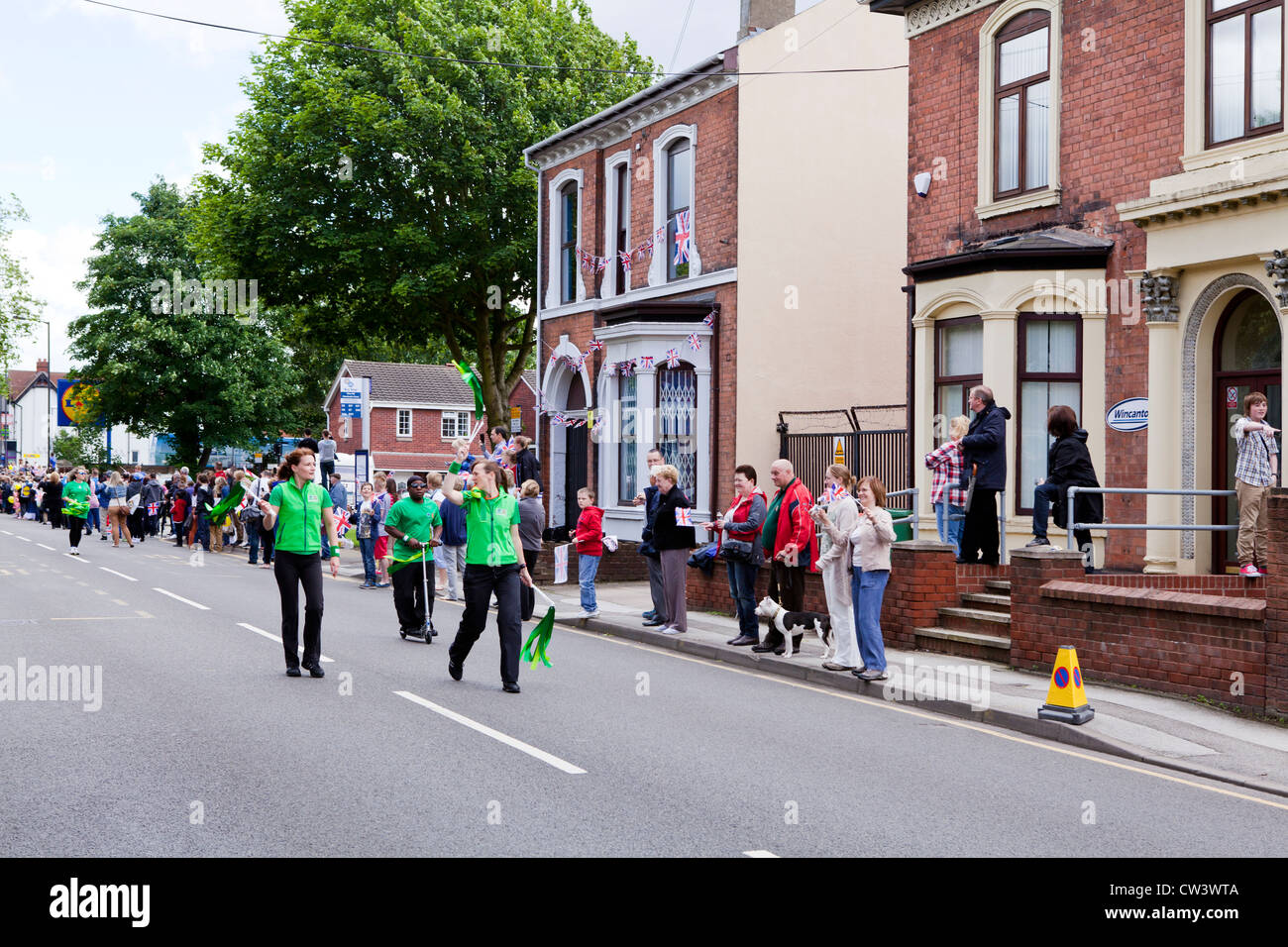 Menschenmengen säumen New Road, Willenhall, West Midlands, um die Weitergabe von die Olympische Fackel und seines Trägers vorangestellt Sponsoren erwarten Stockfoto