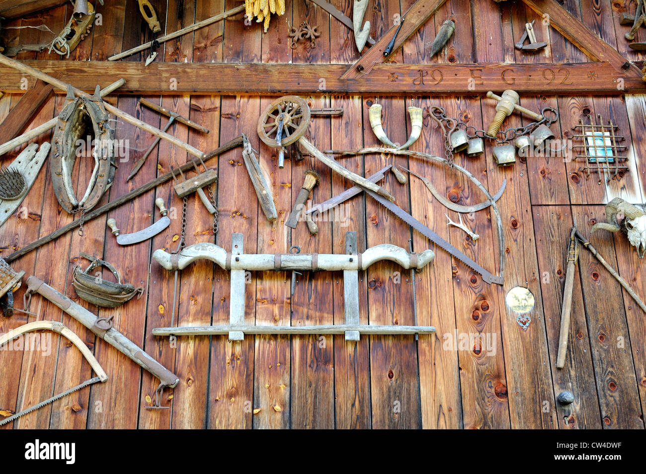 Alte Werkzeuge für die Holzbearbeitung und landwirtschaftliche Geräte fest an der Seite einer hölzernen Scheune in den österreichischen Alpen. Stockfoto