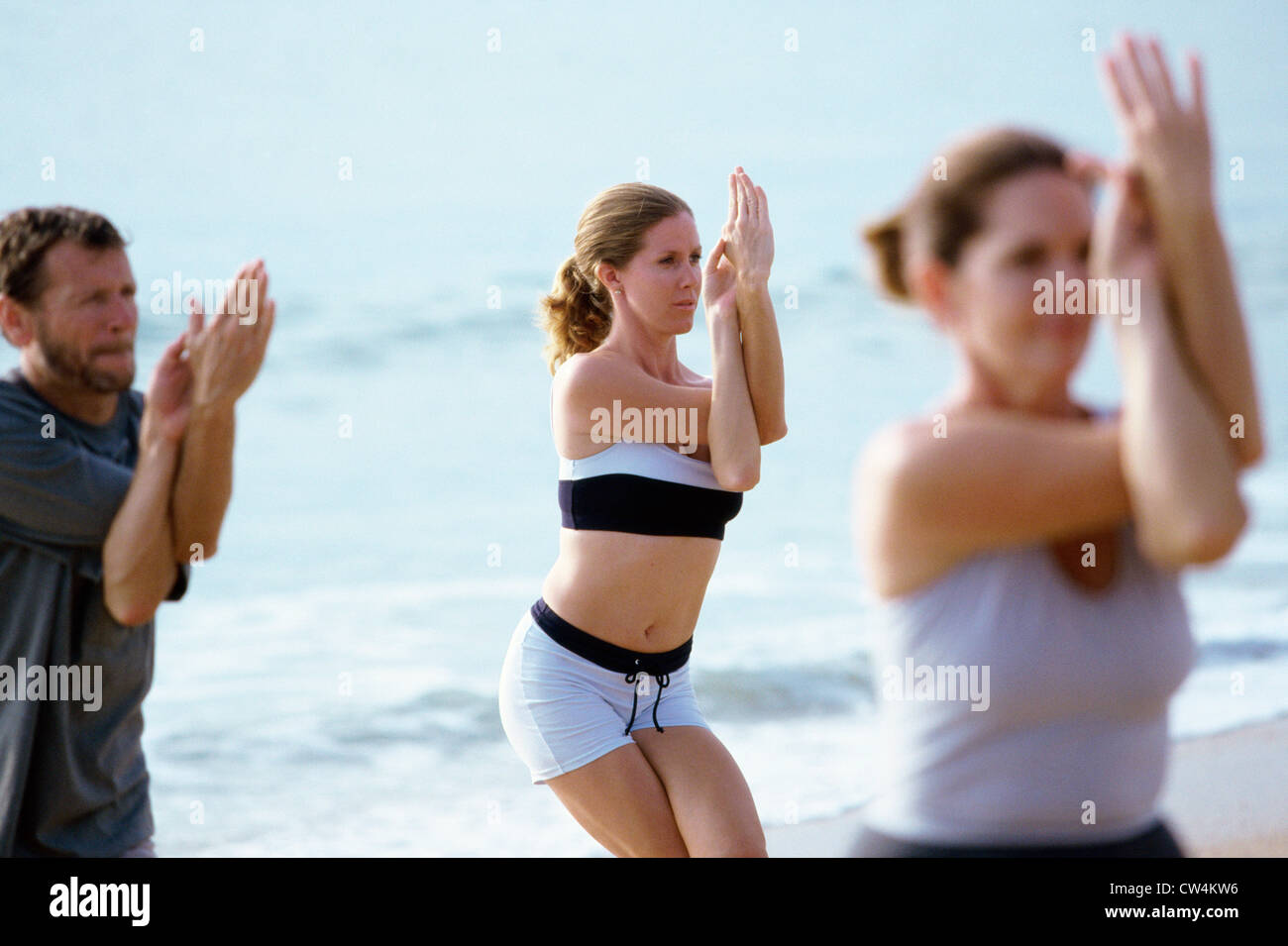 Zwei junge Frauen und ein reifer Mann Training am Strand Stockfoto