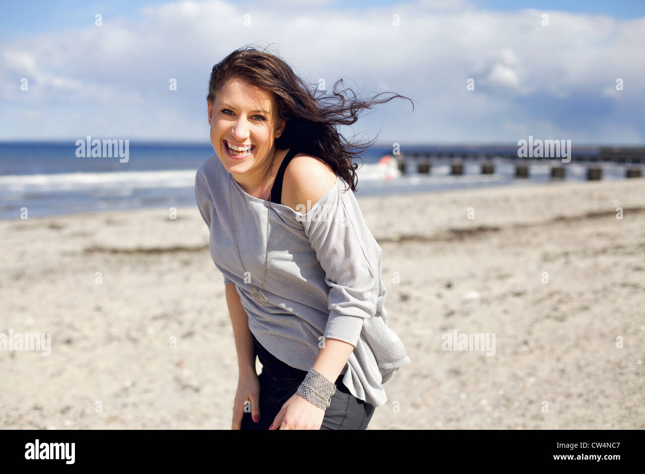 Junge Frau lächelnd und glücklich am Strand gegen den hellen Himmel suchen Stockfoto