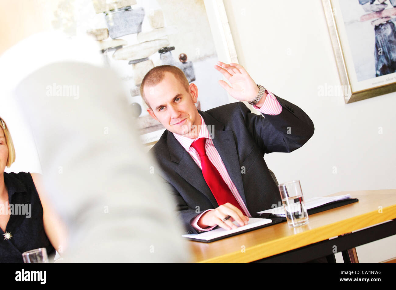 junger Geschäftsmann hebt seine Hand, während ein beheiztes Geschäftstreffen zu stimmen Stockfoto