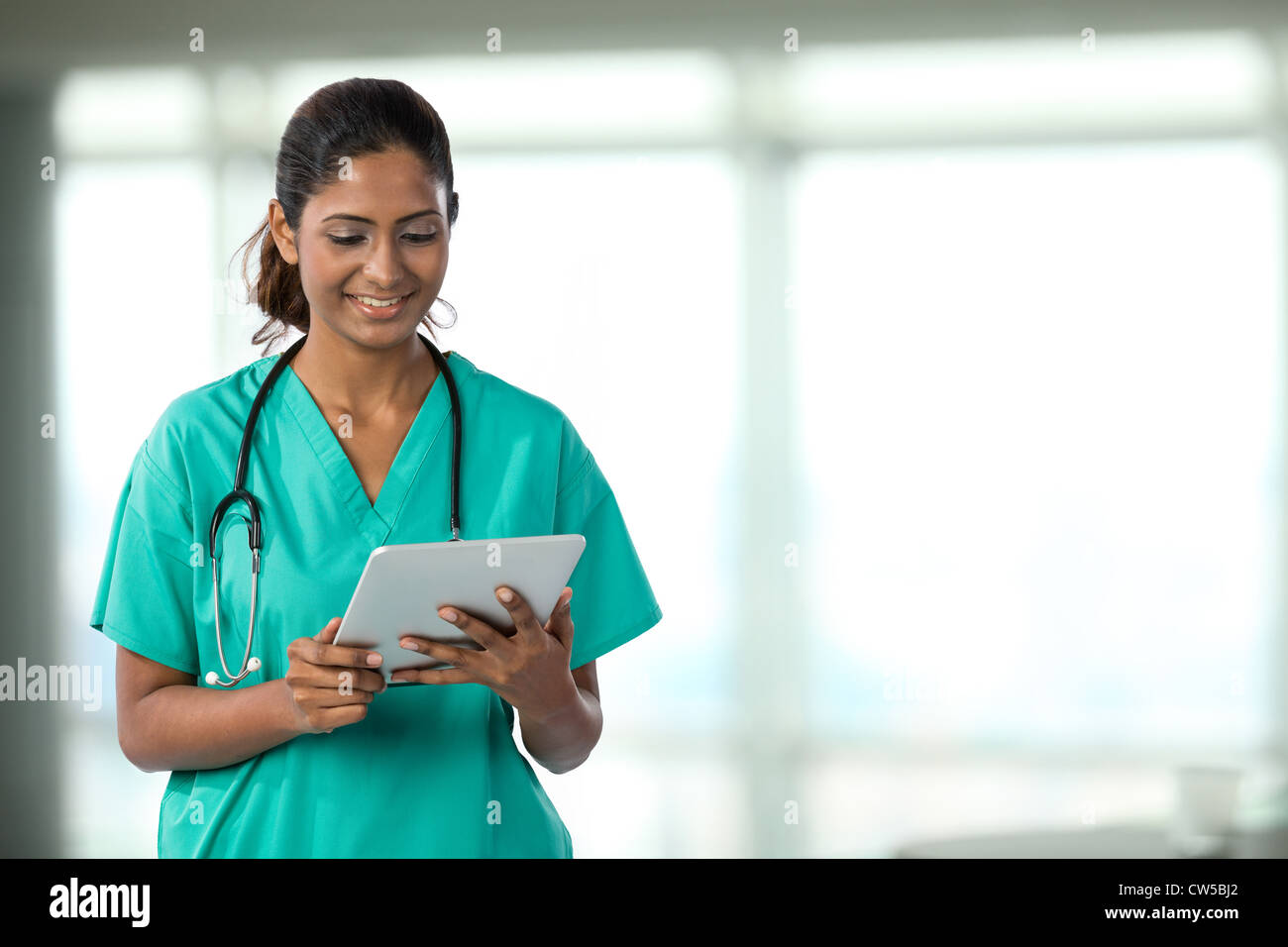 Indische Ärztin Blick auf eine digital-Tablette & tragen scheuert sich ein grünes plus Stethoskop. Stockfoto