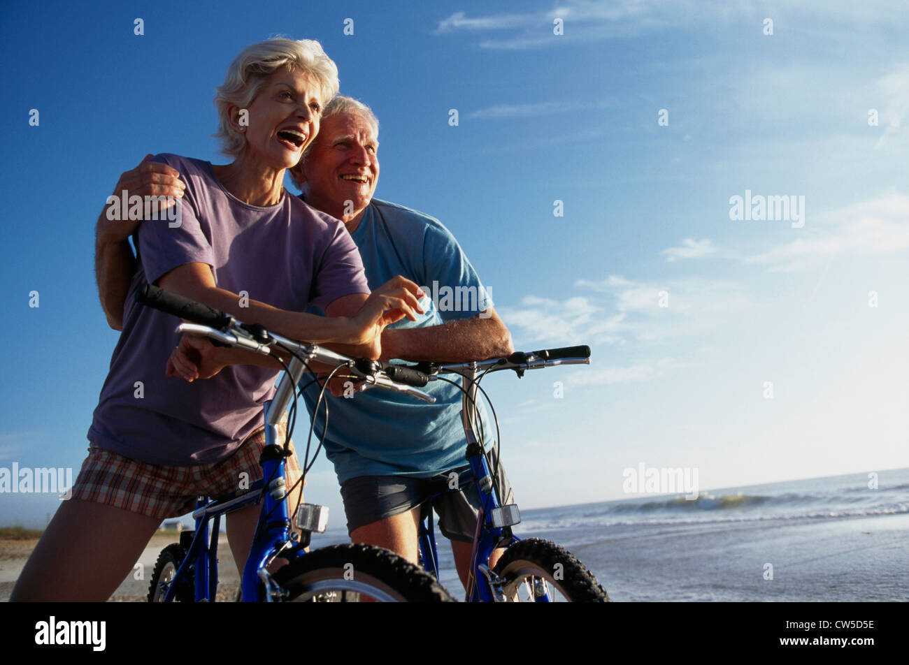 Älteres Paar auf dem Fahrrad sitzen und Lächeln am Strand Stockfoto