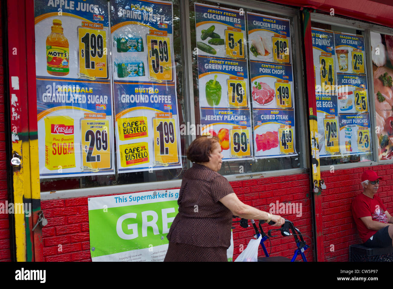 Eine ältere Frau mit einer Gehhilfe übergibt Verkauf Zeichen für Lebensmittel in das Fenster eines Supermarktes Stockfoto