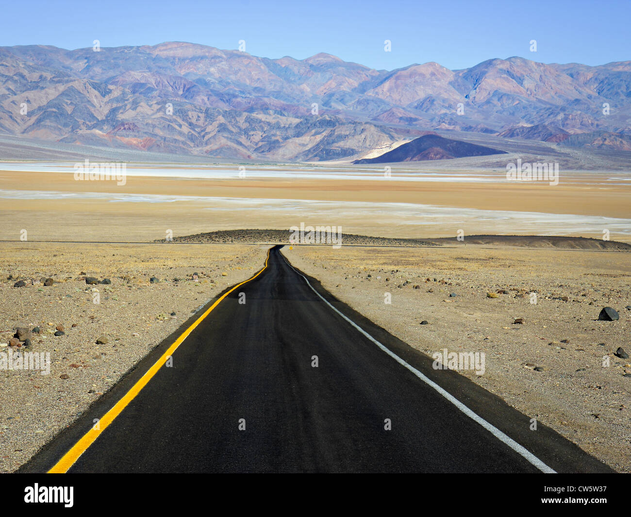 Einspurige Wüstenstraße Abstieg ins Tal mit Salinen und Berge in der Ferne Stockfoto
