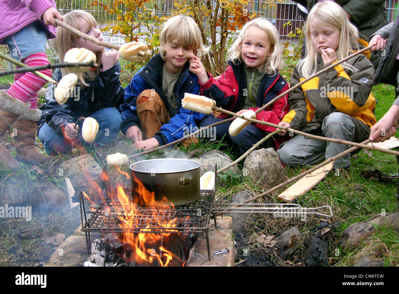 Kinder im Grundschulalter am Lagerfeuer Rösten Brot rollt auf Stöcke und kochende Wasser für Tee, Deutschland Stockfoto