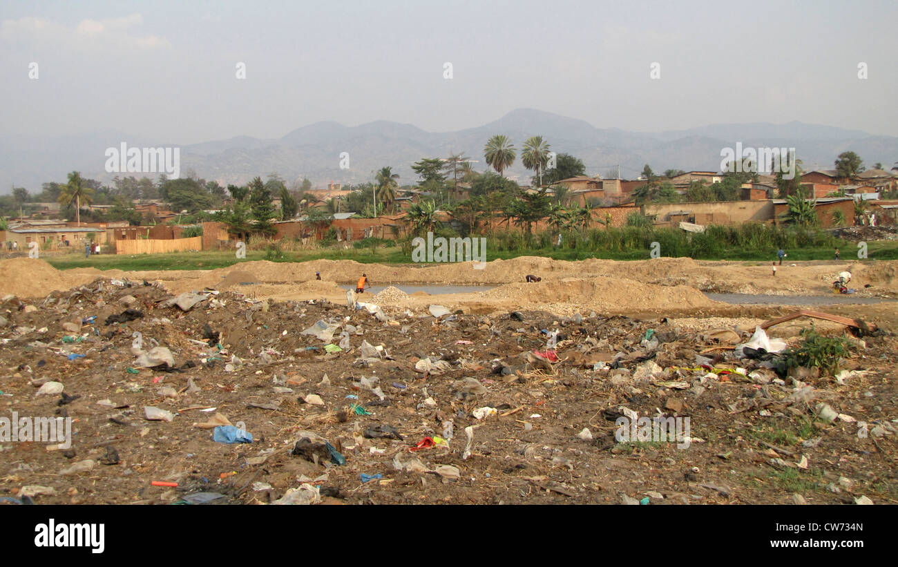 Frauen Waschen von Kleidern und Männer Schaufeln Sand in Eimer an einen Fluss mit Müll bedeckt; im Hintergrund die Elendsviertel der Hauptstadt Burundis, Bujumbura Mairie, Buyenzi, Bujumbura Stockfoto