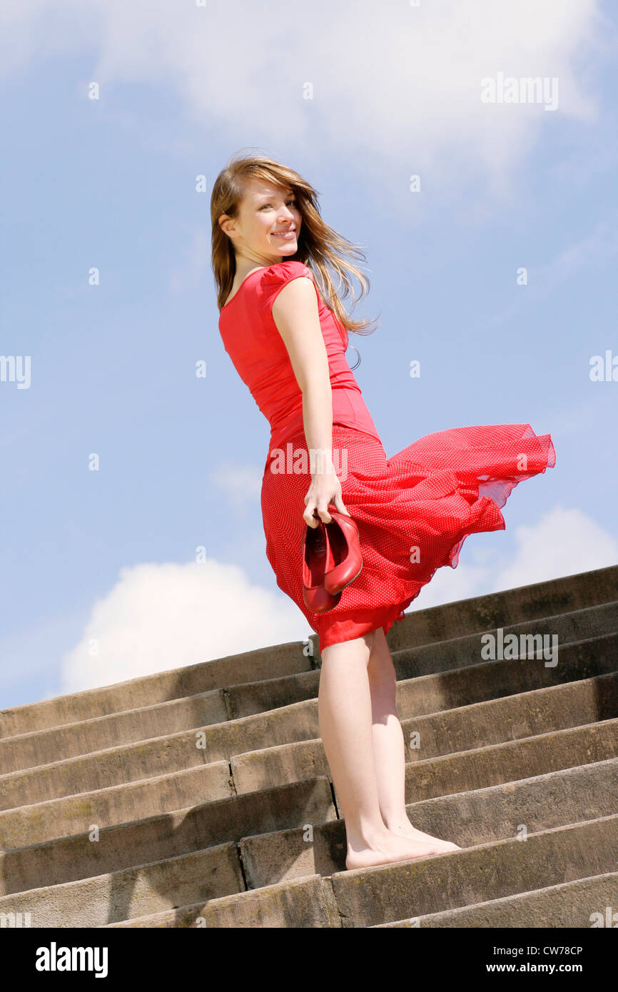 junge Frau in einem roten Kleid, barfuß auf Treppe stehend Stockfoto