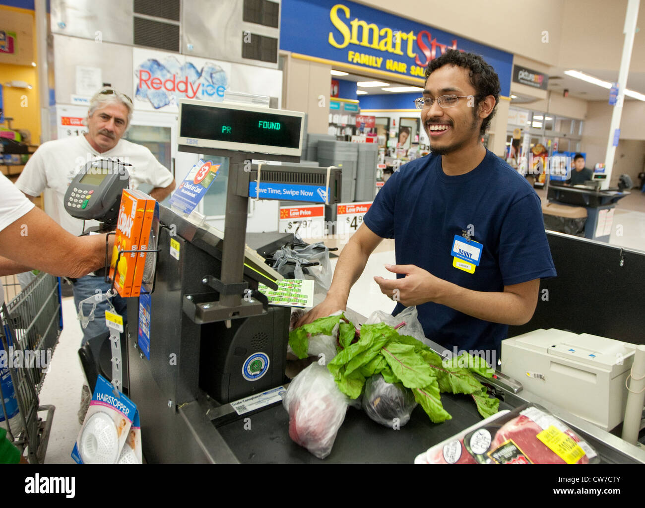 Lächelnde junge Hispanic männlichen Kasse klingelt Produkte für Kunden auf ein Wal-Mart Supercenter in San Marcos, Texas Stockfoto